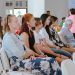A diverse group of people sitting attentively during an indoor meeting or event, captured in a spacious room.